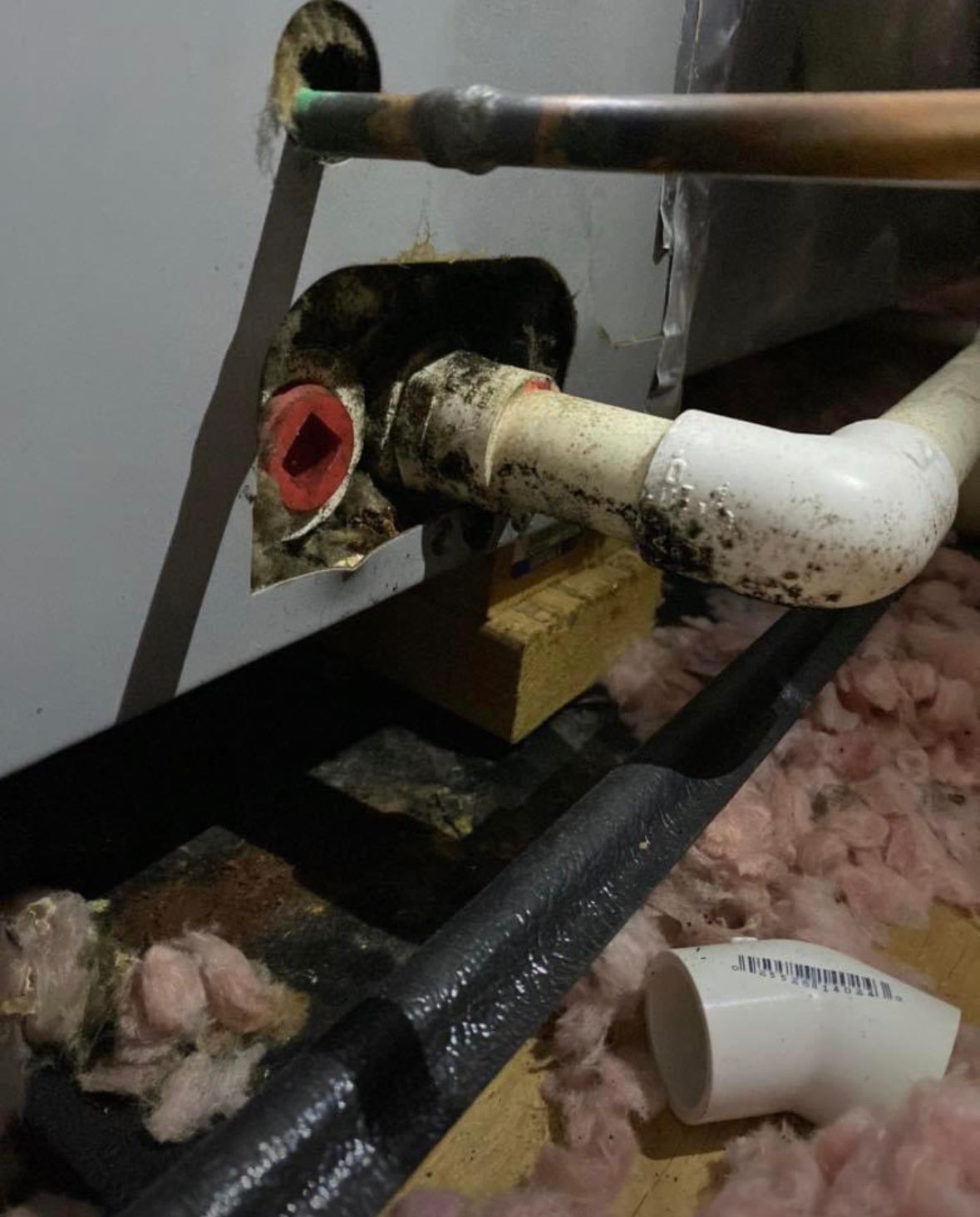 Plumbing pipes with insulation material on the floor underneath a wall opening.